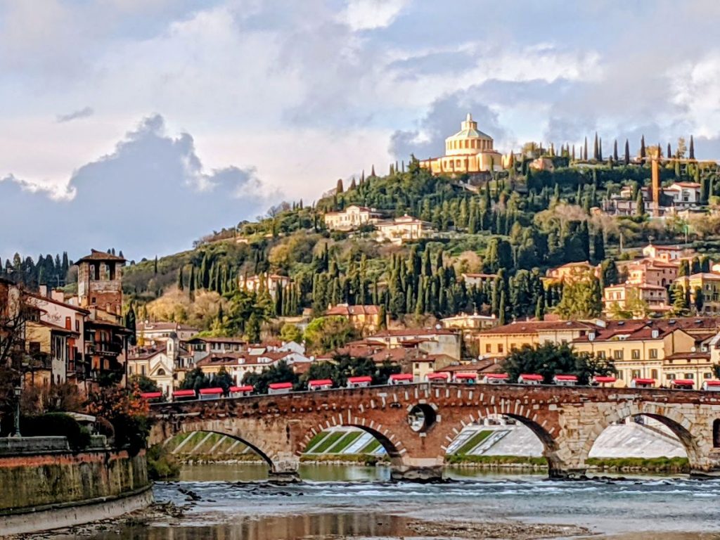 A bridge over the Adige River, with hills in the background.