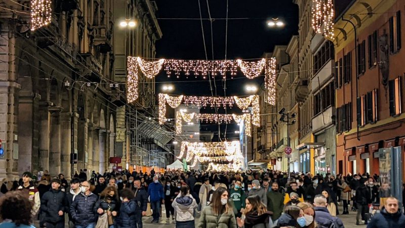 Via Rizzoli, full of shoppers, with Christmas lights strung from one side to the other.