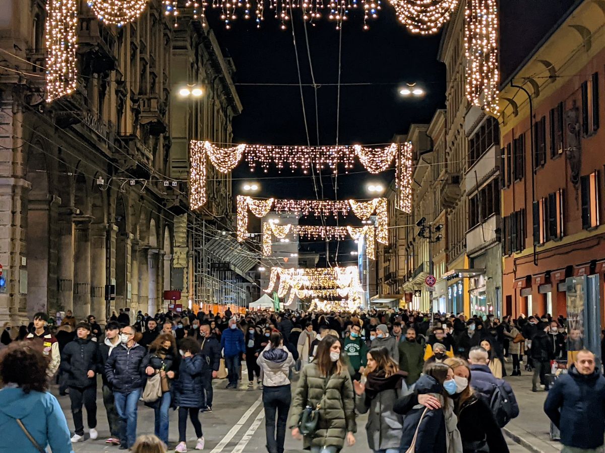 Via Rizzoli, full of shoppers, with Christmas lights strung from one side to the other.