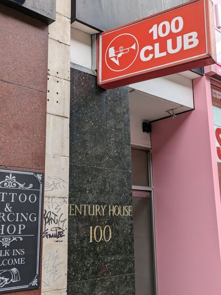 Sign with "100 Club" and a line-art drawing of a trumpeter.